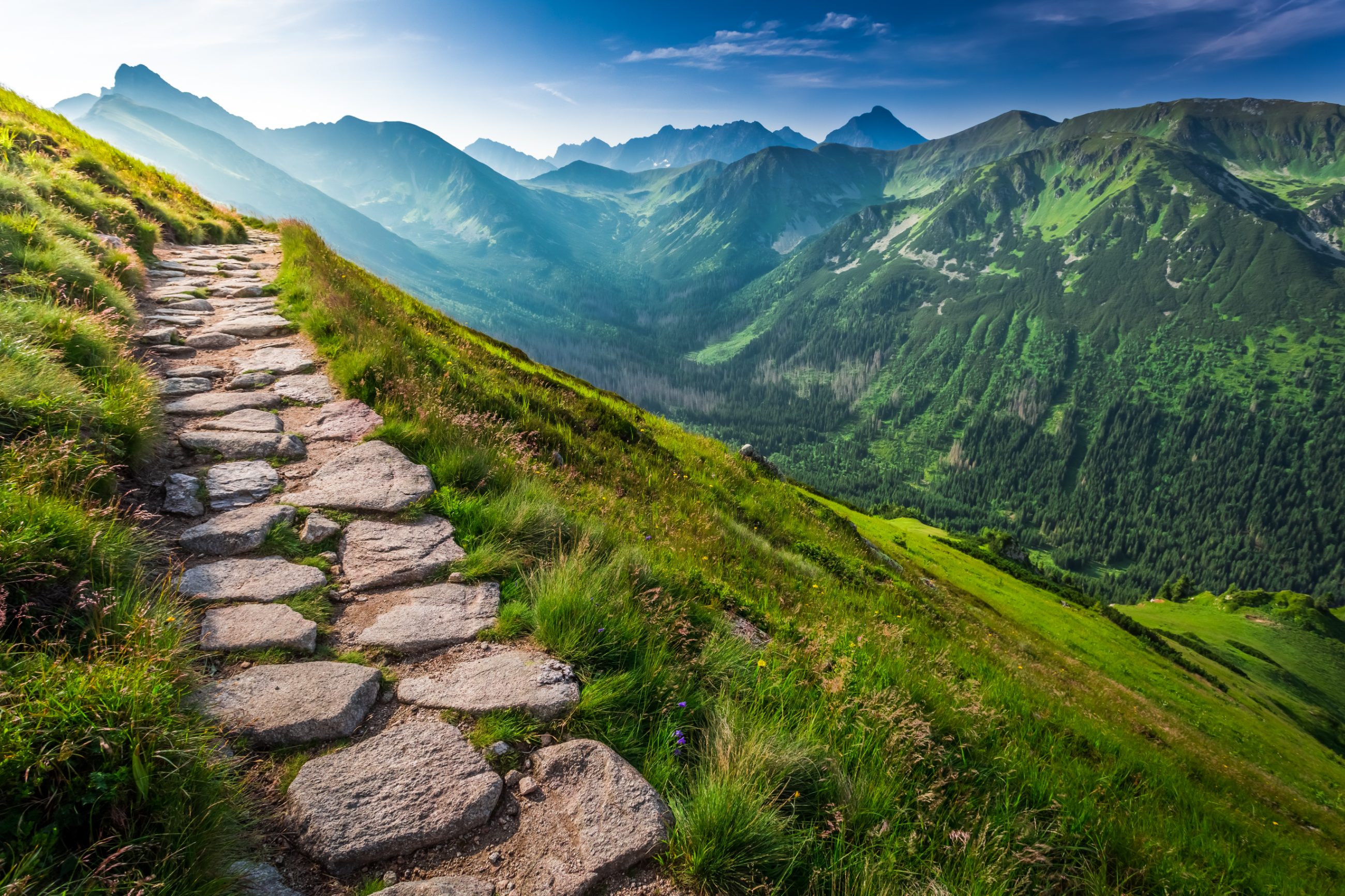 A stone footpath along a ridge in the Tatras mountains at sunrise, opening onto a wide valley